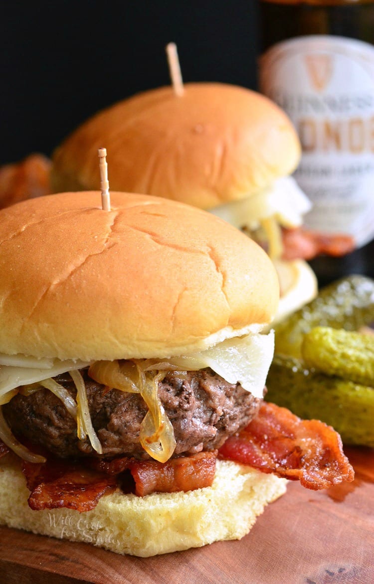 side view of two burgers with onion, cheese, and bacon. 