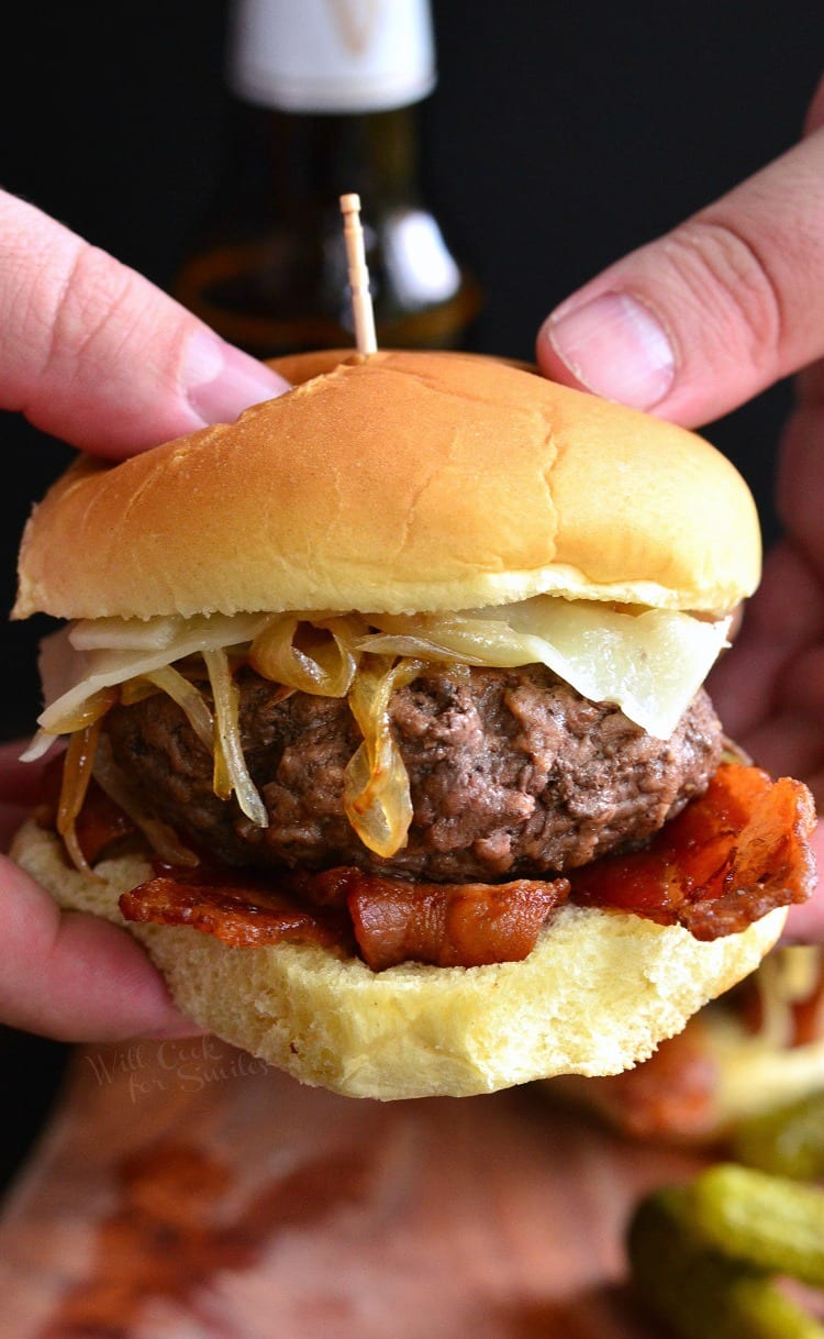 holding burger that has bacon, onions, and cheese with a toothpick in the middle 