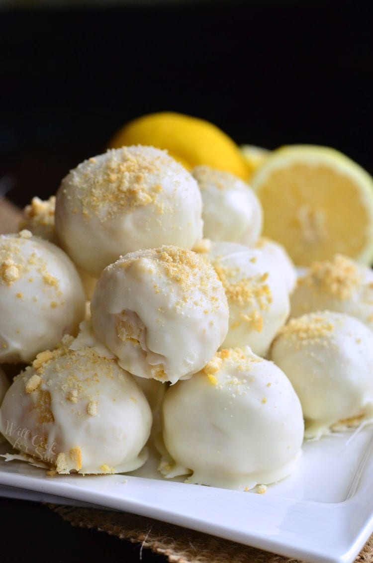 Lemon Oreo Coconut Cookie Truffles stacked up on a white plate with lemons in the background 