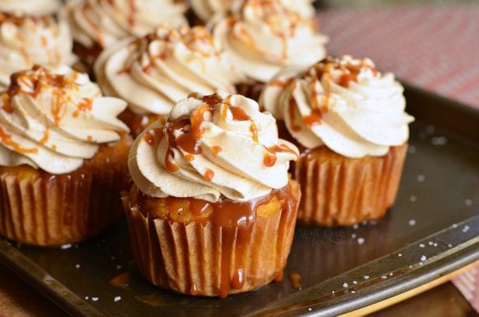 Caramel cupcakes topped with swirls of frosting and drizzled with caramel sauce are neatly arranged on a baking tray.