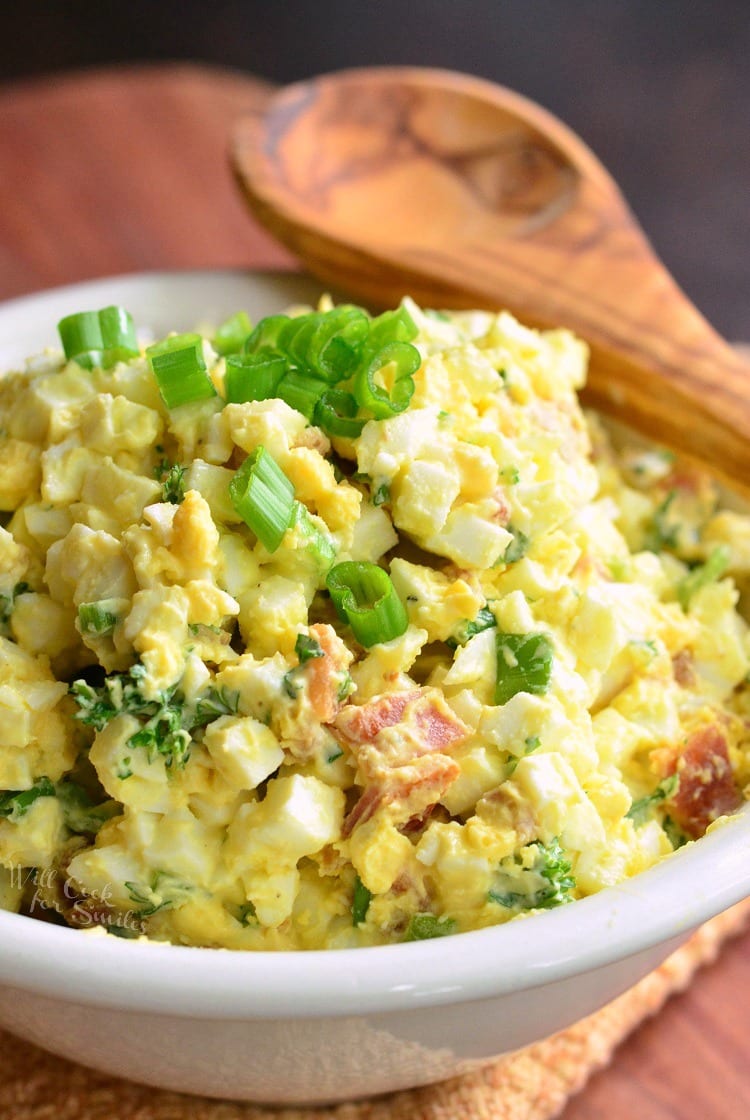 Bacon and Green Onion Egg Salad in a white bowl with a wooden spoon across the top 