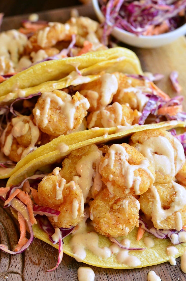 three corn tortillas filled with crispy shrimp and cabbage with sour cream on top.