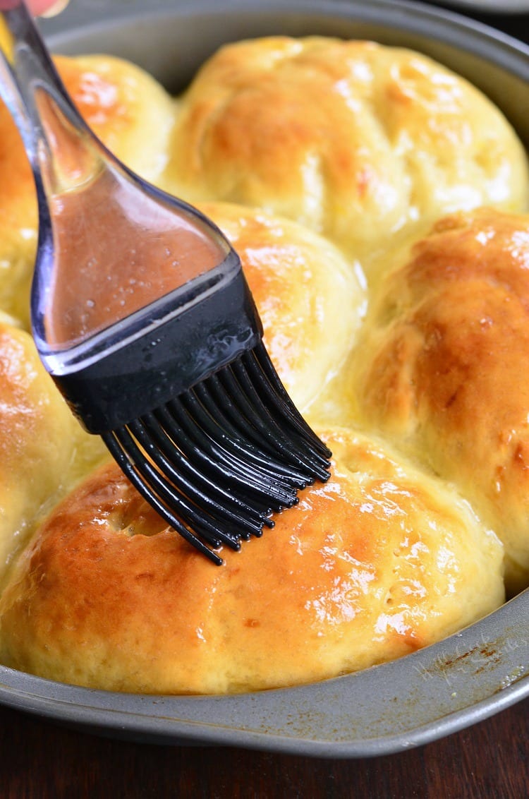 brushing Honey Lemon Dinner Rolls in a baking dish with butter 