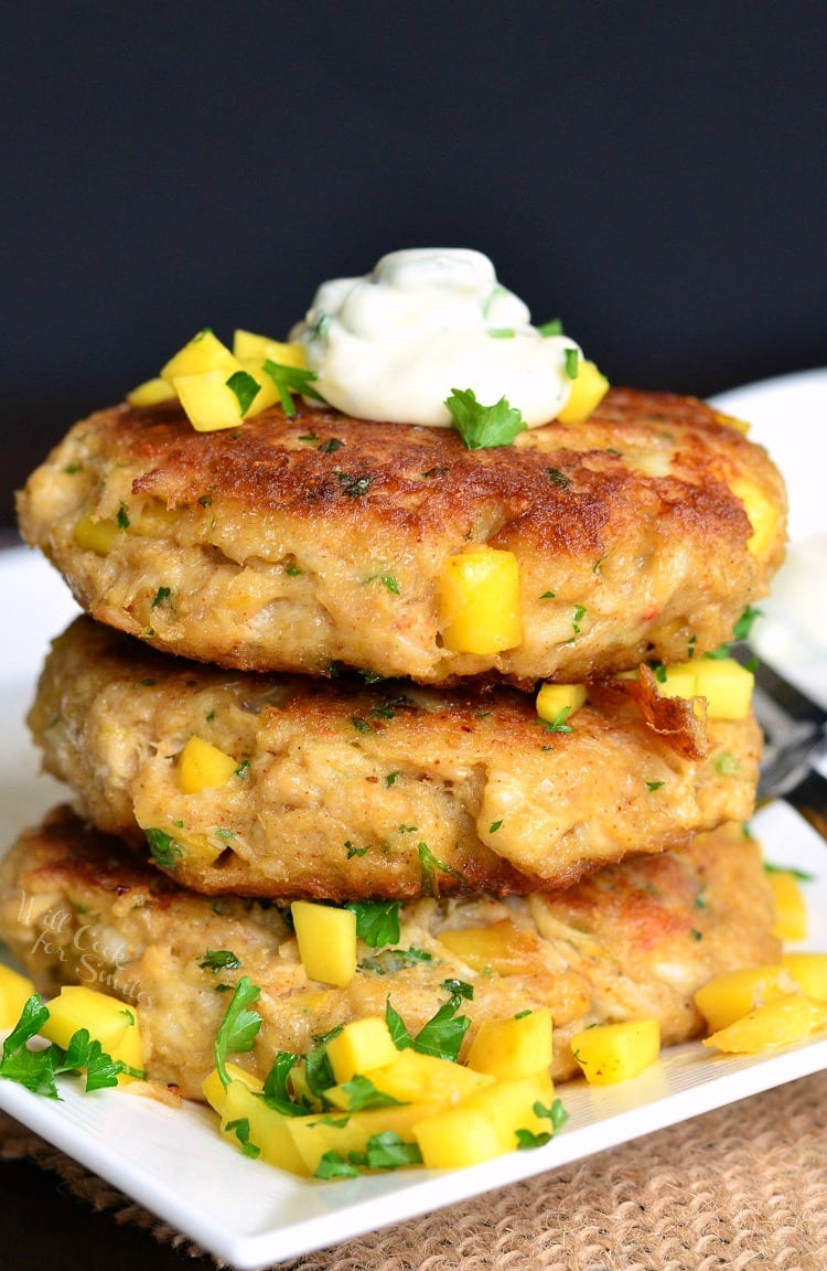 Spicy Mango Crab Cakes stacked on a plate with sour cream on top and diced mango and parsley on the plate 