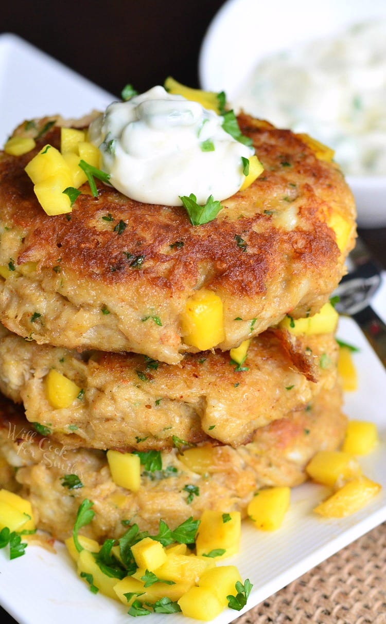 stacked three large mango crab cakes with some fresh mangoes dices on top and creamy topping.