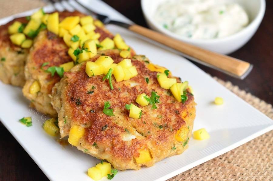 3 Spicy Mango Crab Cakes on a plate with diced mango and parsley and a fork 