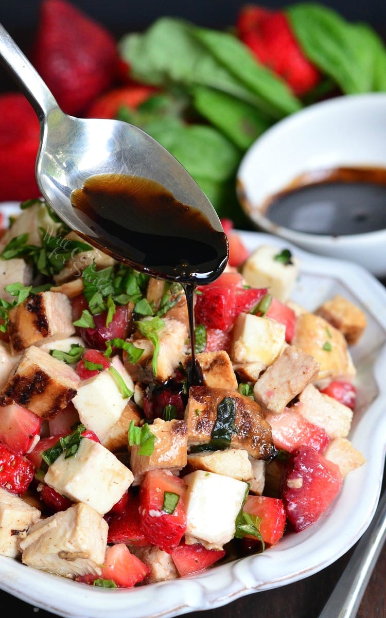 Balsamic Strawberry Chicken Salad in a white bowl with dressing being spooned over it 