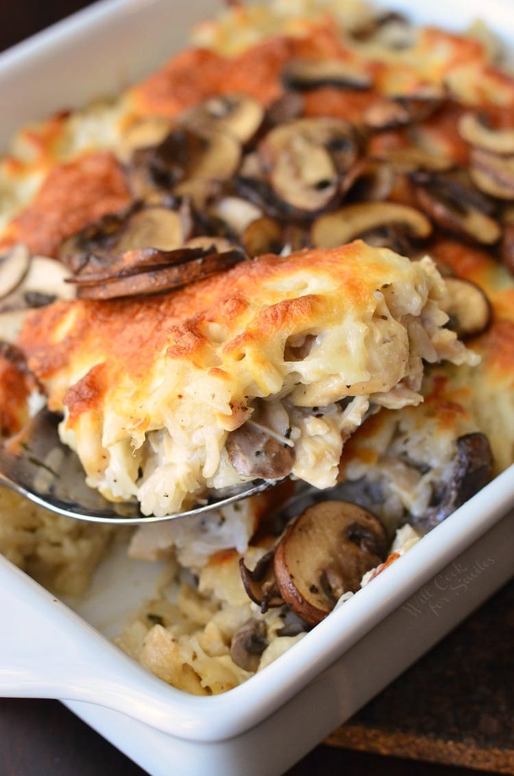 lifting Creamy Chicken Mushroom Rice Casserole in a white baking dish out with a spoon 