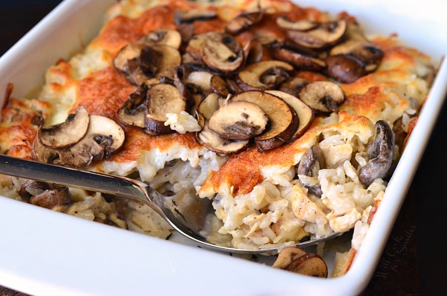 spooning Creamy Chicken Mushroom Rice Casserole in a white baking dish 