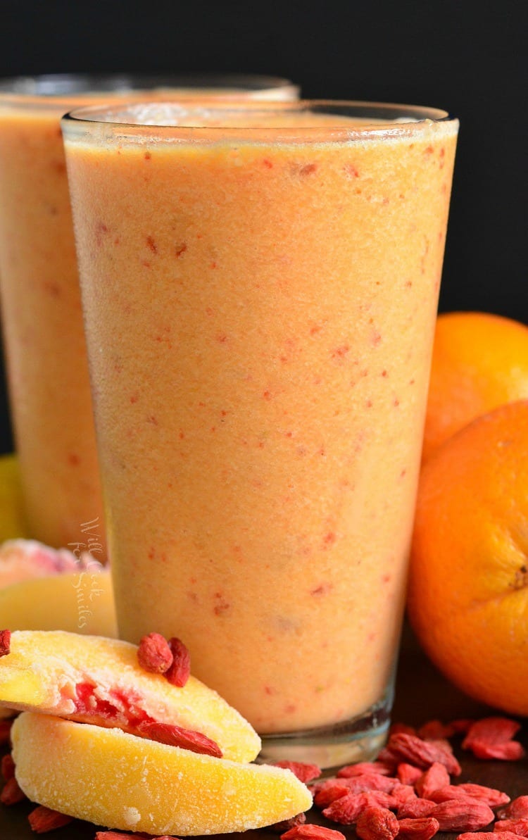 Creamy Peach and Goji Berry Smoothie in two glasses with peaches and goji berry on the table around it 