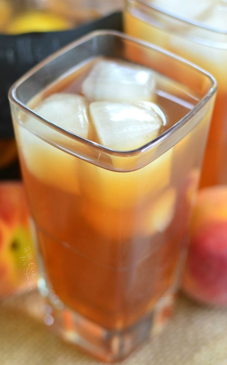 Top view Grilled Lemon Peach Iced Tea in a glass with ice and peaches in the background 