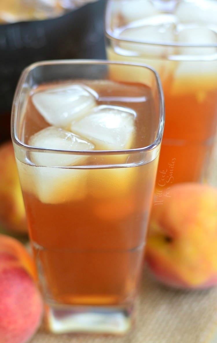Grilled Lemon Peach Iced Tea in a glass with ice and peaches in the background 