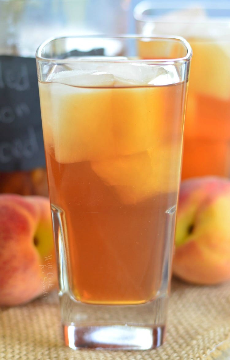 Grilled Lemon Peach Iced Tea in a glass with ice and peaches in the background 
