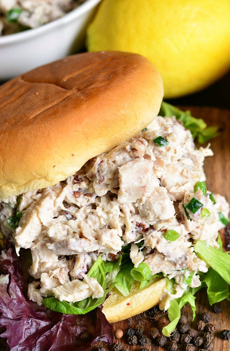 Lemon Pepper Rotisserie Chicken Salad on a bun on a cutting board with peppercorns around it and a lemon in the background 