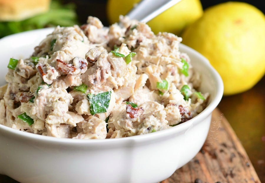 Lemon Pepper Rotisserie Chicken Salad in a white bowl on a table with lemons in the background 