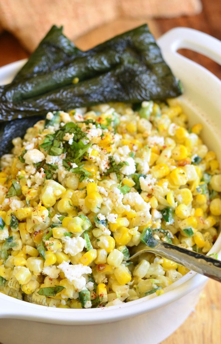 close up of corn salad in a white bowl with a fork inside it.