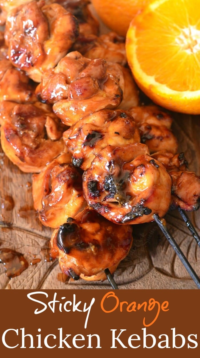 Sticky Orange Chicken Kebabs stacked up on a cutting board with a cut lemon on the side 