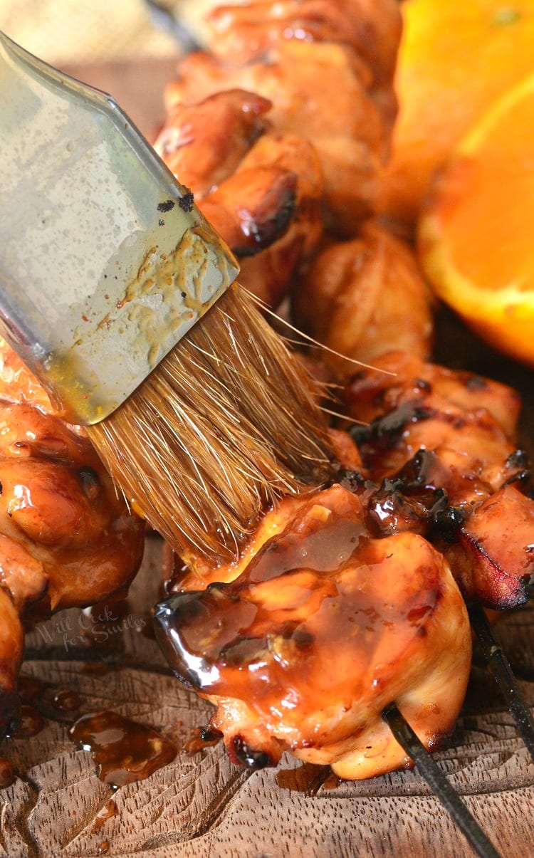 brushing Sticky Orange sauce onto Chicken Thigh Kebabs that are on a cutting board 