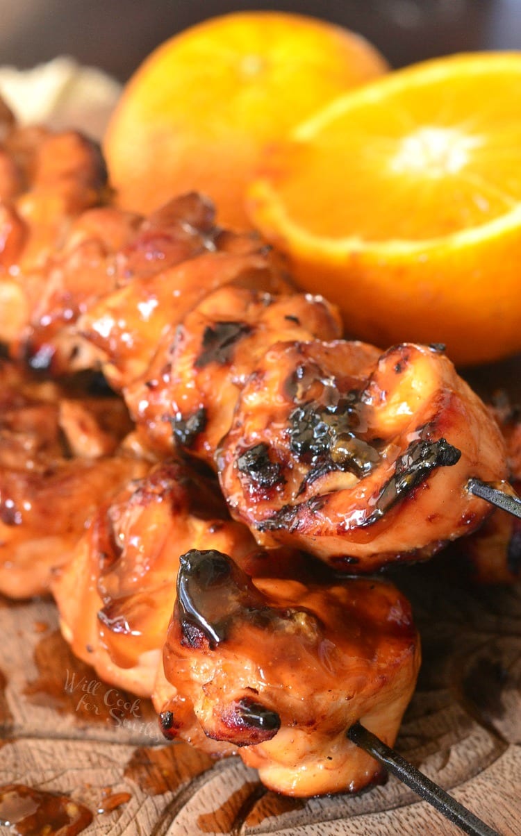 Sticky Orange Chicken Kebabs stacked up on a cutting board with a cut lemon on the side 