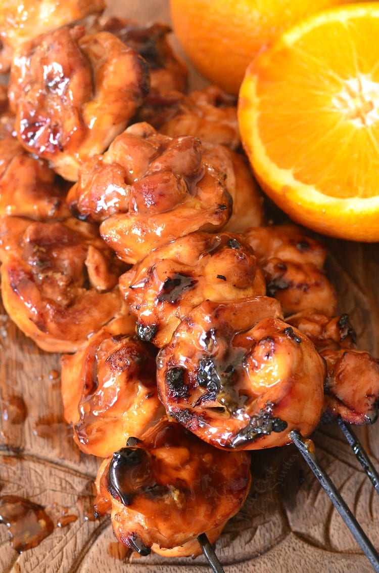 Sticky Orange Chicken Kebabs on a wood cutting board with a orange that is sliced in half 