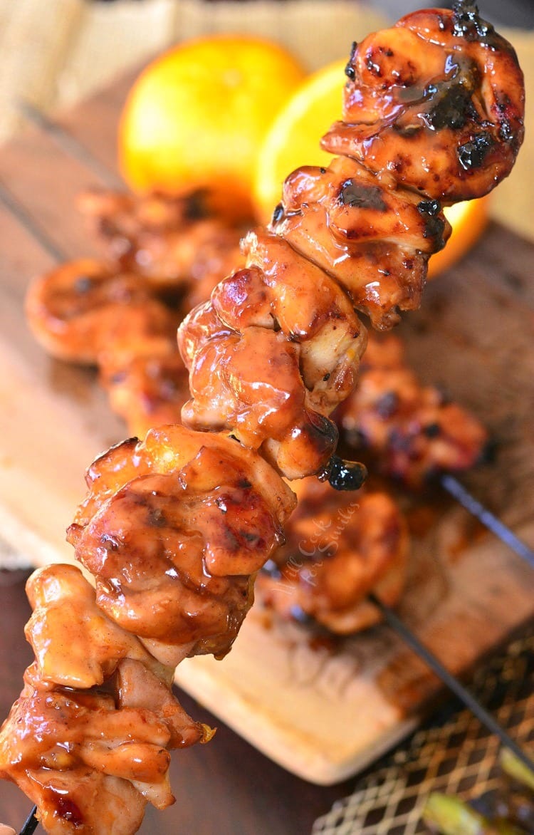 Lifting up a Sticky Orange Chicken Kebabs stacked up on a cutting board with a cut lemon on the side 