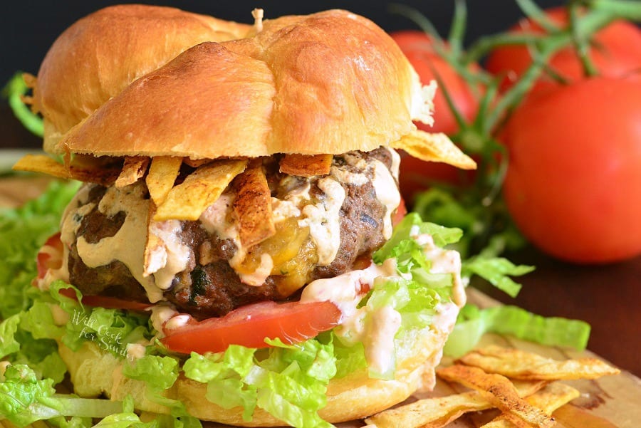 Stuffed Taco Burger on a bun with lettuce and tomato with tomato in the background 