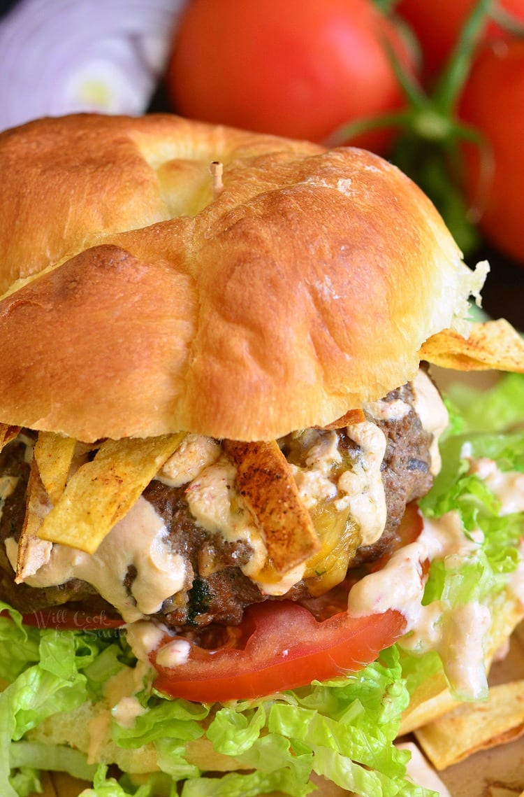 Stuffed Taco Burger on a bun with lettuce and tomato with tomato in the background 