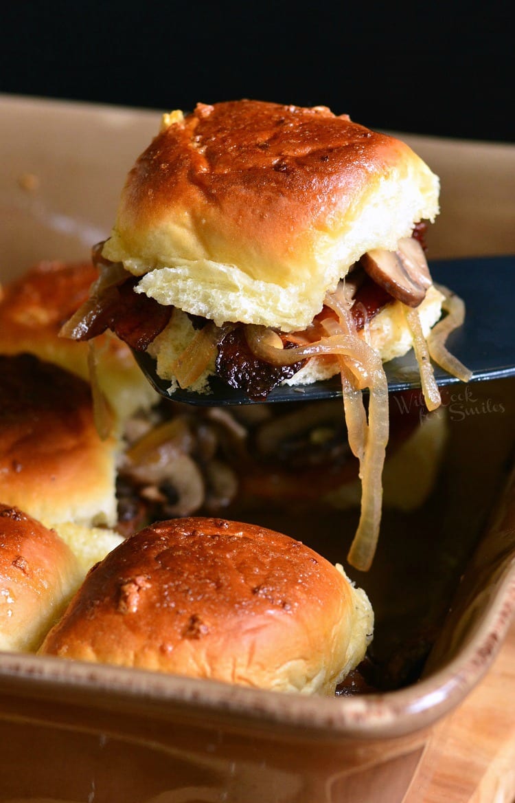 Bacon Mushroom and Onion Sliders in a baking dish with a spatula lifting one out 