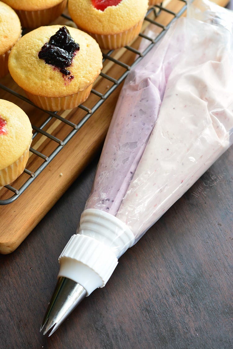 Cupcakes with strawberry and blueberry jam with a piping bag of frosting next to it.