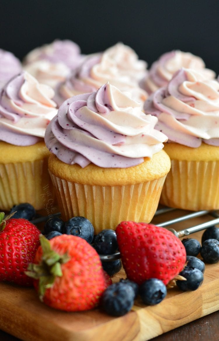 cupcakes with strawberry and blueberry swirl frosting on a cooling rack.