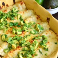 Vegetable Enchiladas in a yellow casserole dish with avocado and cilantro on top.