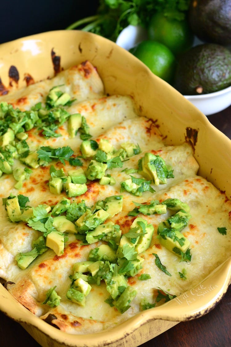Cheesy Vegetable Enchiladas in a yellow backing dish with diced avocado and cilantro on top 