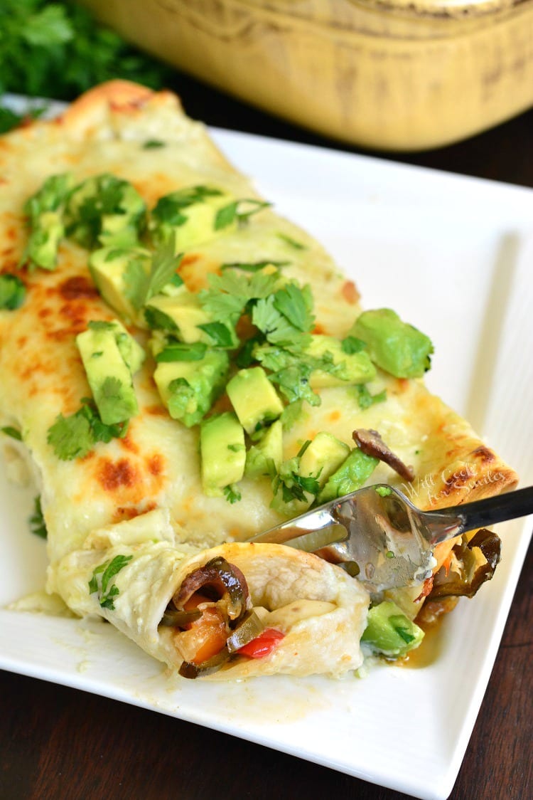two enchiladas on a plate with avocado and cilantro on top