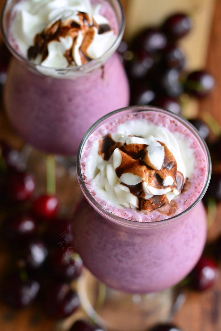 2 Chocolate Covered Cherry Milkshakes with whip cream and chocolate on top with cherries on a table 