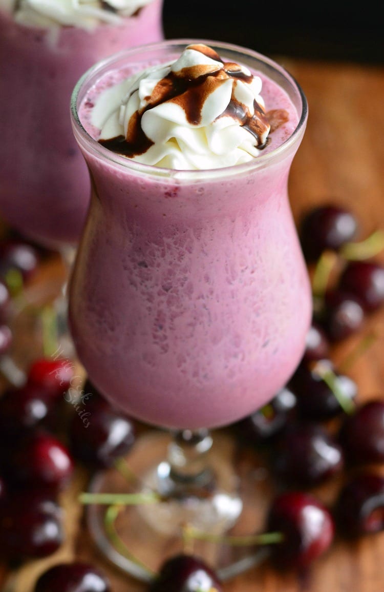 Chocolate Covered Cherry Milkshake with whip cream and chocolate on a table with cherries around it