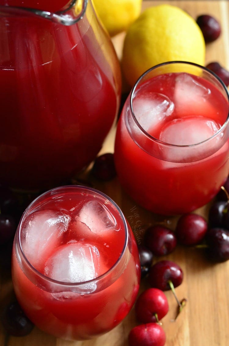 Top view of Cherry Arnold Palmer in glasses with a pitcher to the left of them with cherries around them and lemons on a cutting board 