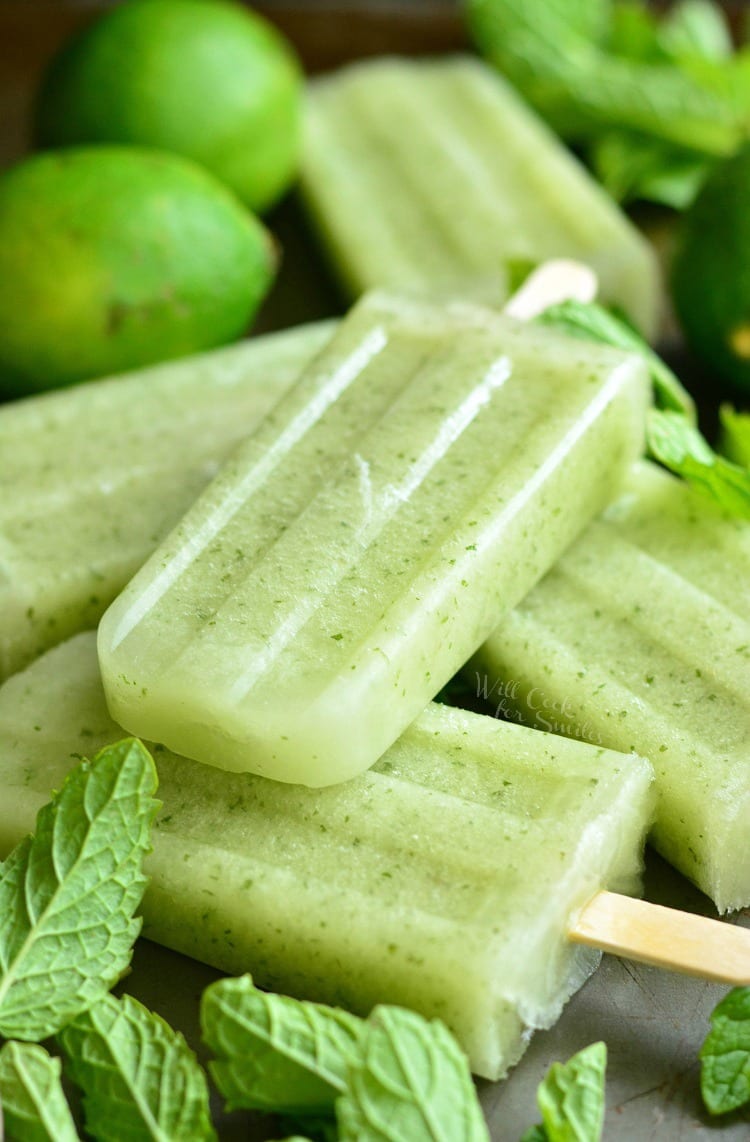 Honeydew Mojito Popsicles staked on a cutting board with mint leaves and lemons in the background 