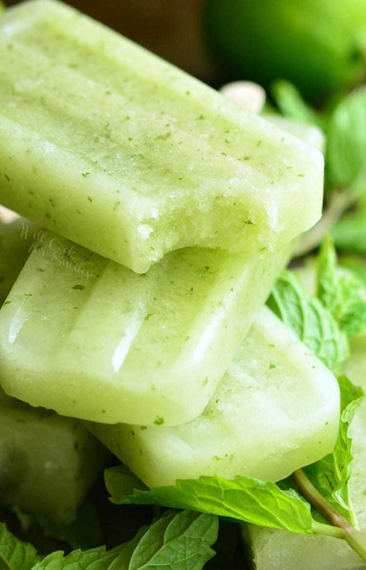 Honeydew Mojito Popsicles, one with a bite taken out, staked on a cutting board with mint leaves 