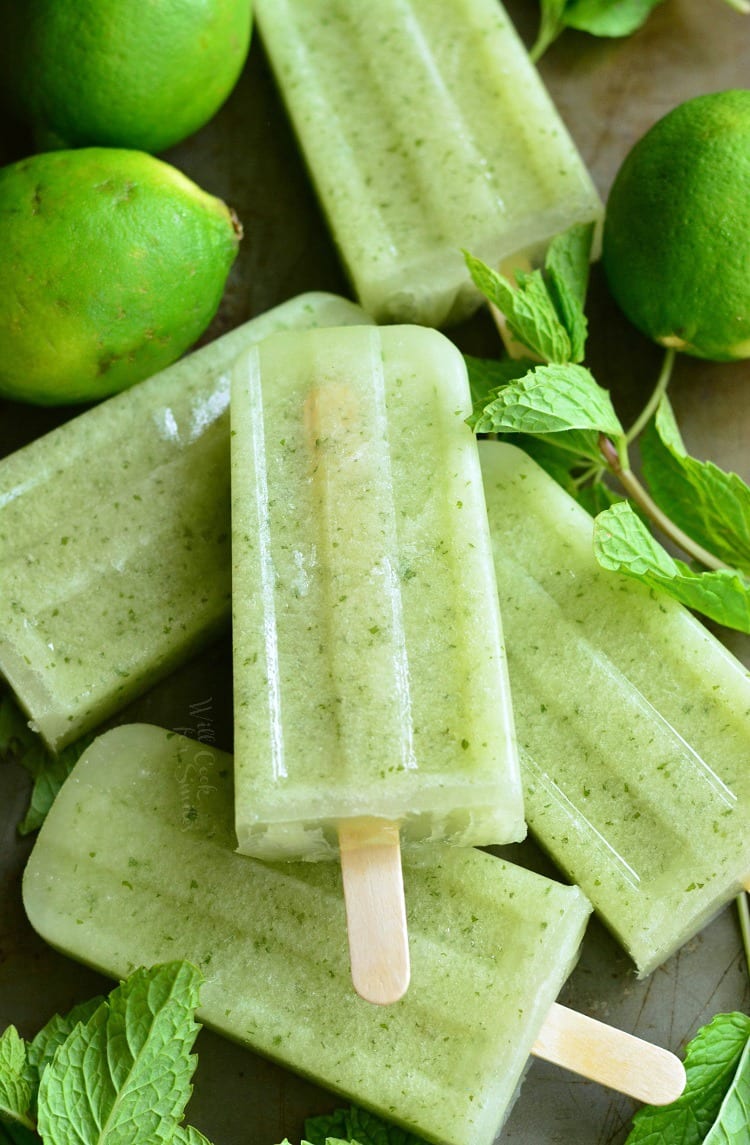 Honeydew Mojito Popsicles steaked on a cutting board with mint leaves and lemons in the background 