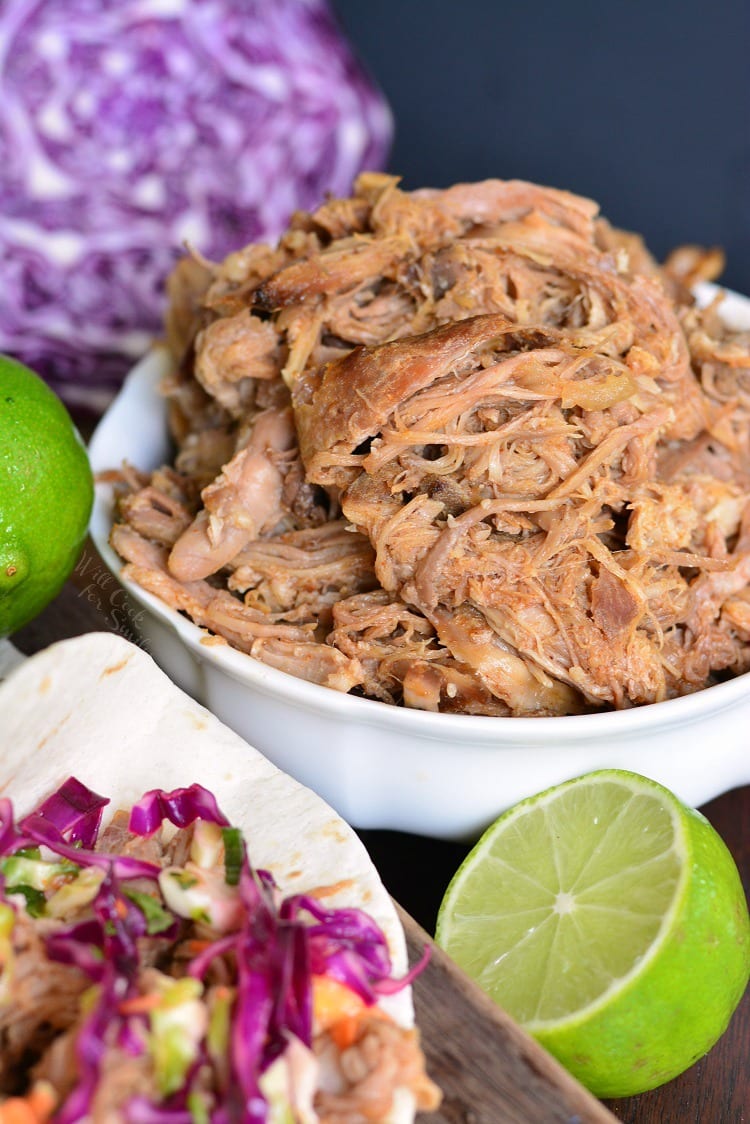 Pulled Pork in a bowl with cabbage and limes around it 