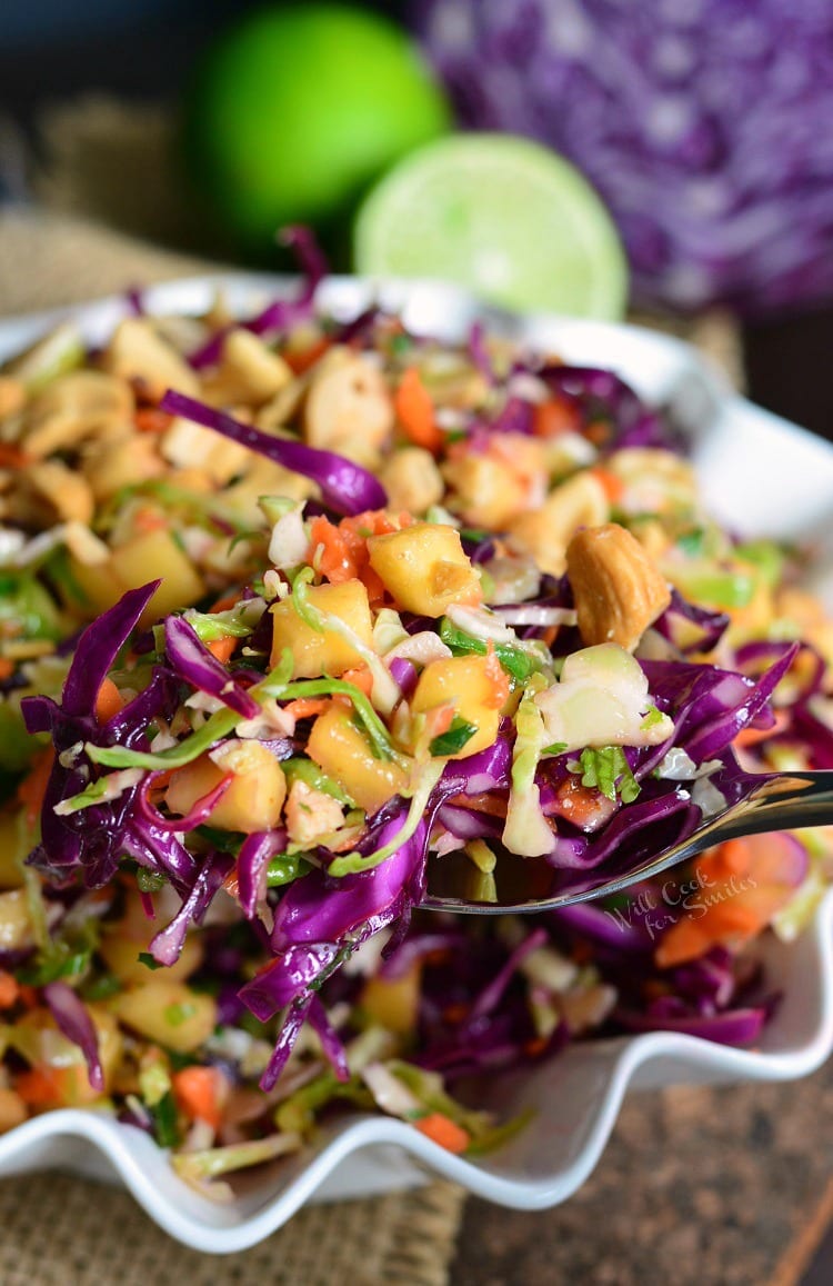 Scooping tropical Slaw in a white serving bowl out with a spoon and a lime in the background 