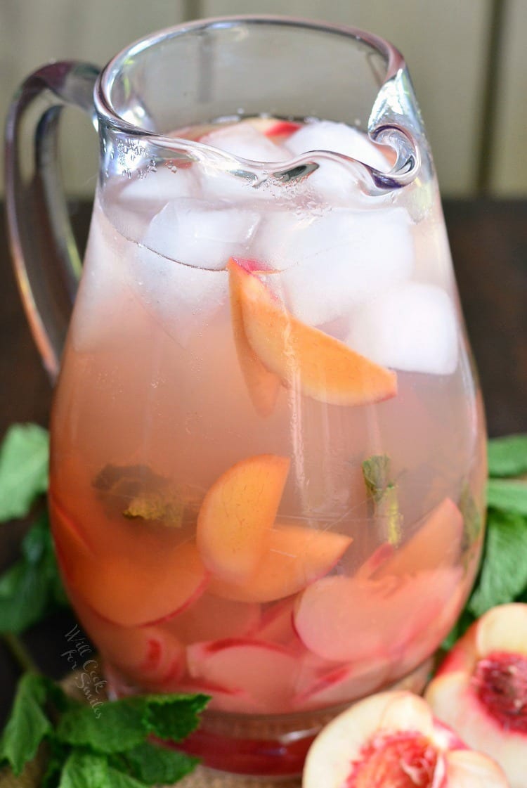 Mint Peach Rose Spritzer in a pitcher on a table with a peach cut in half 
