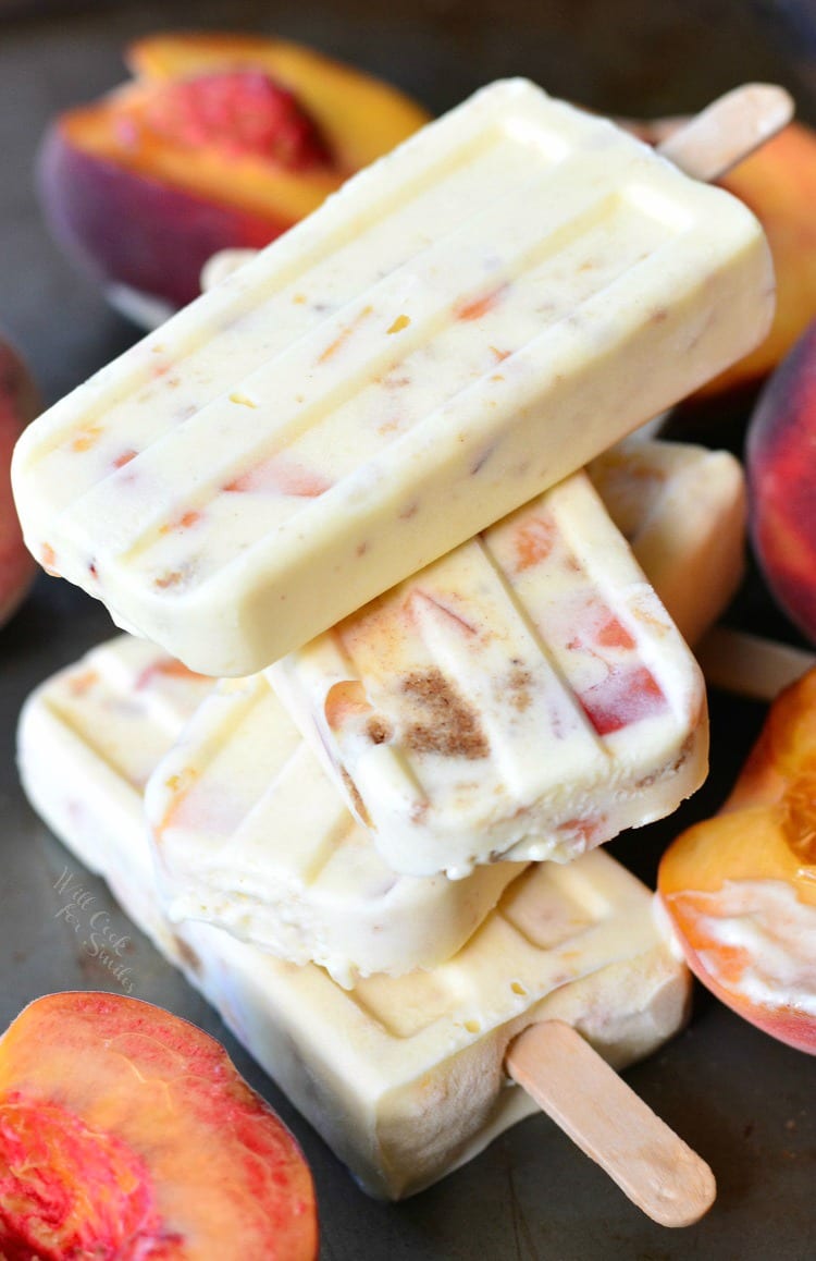 4 Peach Cobbler Pudding Pops stacked up on a table with peaches around them 