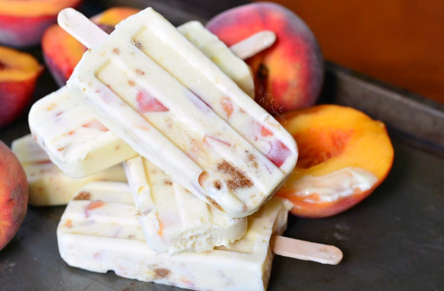 4 Peach Cobbler Pudding Pops stacked up on a table with peaches around them 