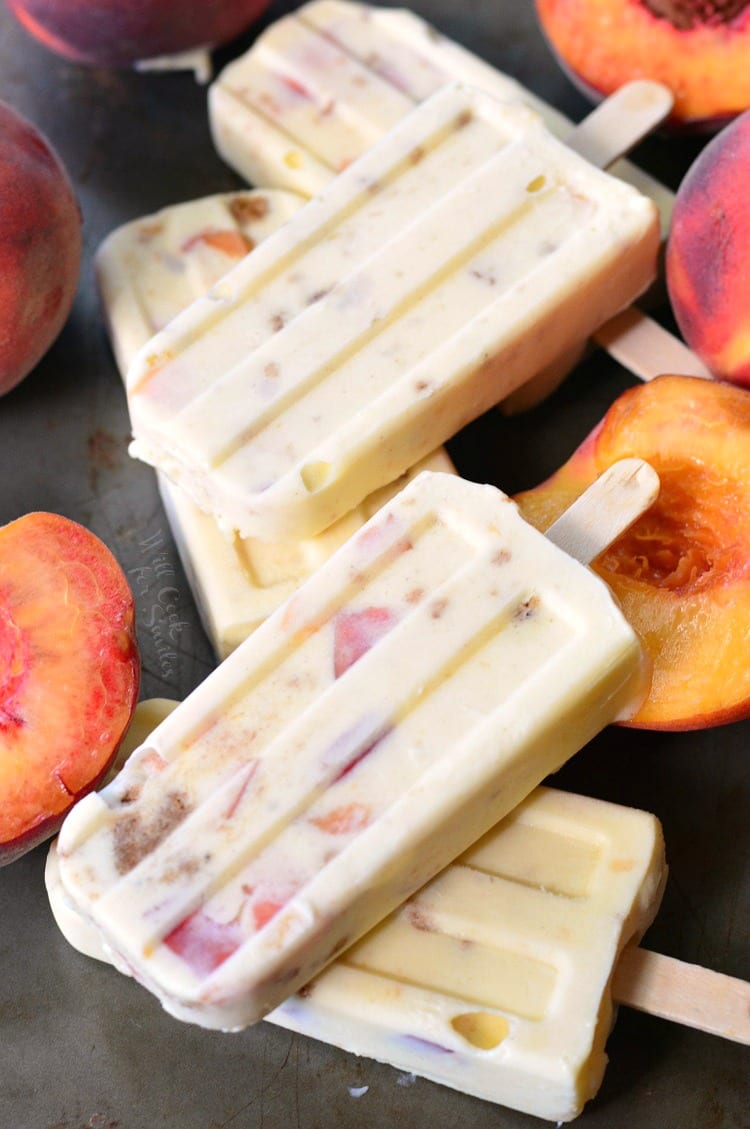 4 Peach Cobbler Pudding Pops stacked up on a table with peaches around them 