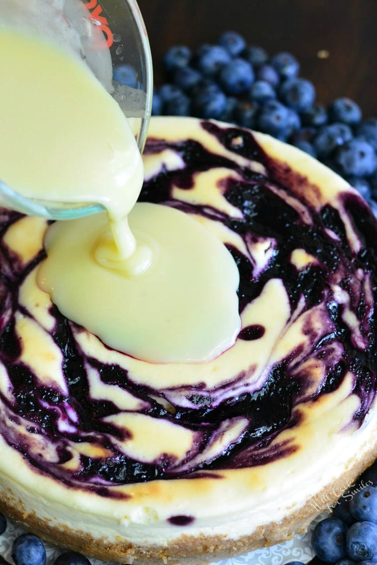 pouring white chocolate over a blueberry cheesecake.