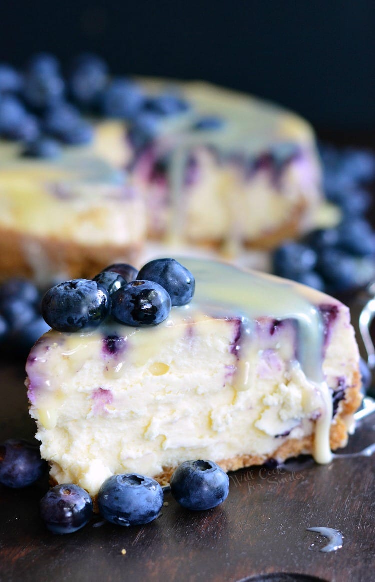 slice of cheesecake with blueberries and white chocolate sauce on top.