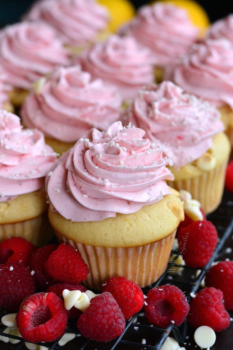 White Chocolate Lemon Cupcakes with Raspberry Frosting on a cutting board with raspberries around it