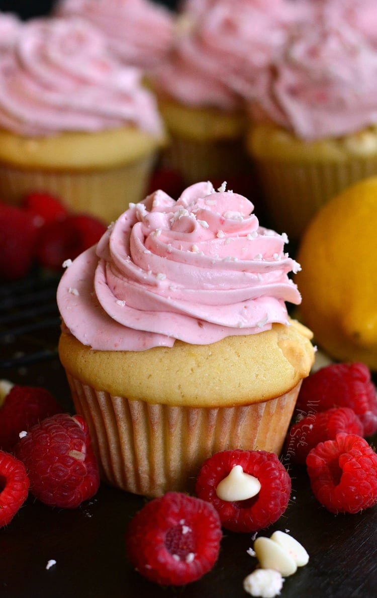 Cupcake with pink frosting and raspberries around the bottom of it.