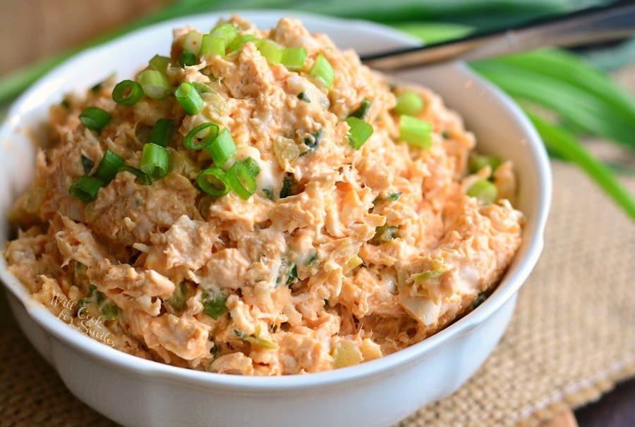 Zesty Buffalo Chicken Salad in a white bowl with green onions on top and fork, on a table 